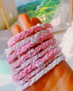 a hand is holding several pink and white bracelets with words written on the beads