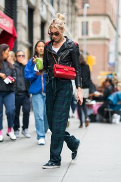 a woman walking down the street while wearing plaid pants and a black leather jacket with a red handbag