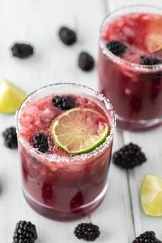 two glasses filled with raspberry lemonade and blackberries on top of a white table