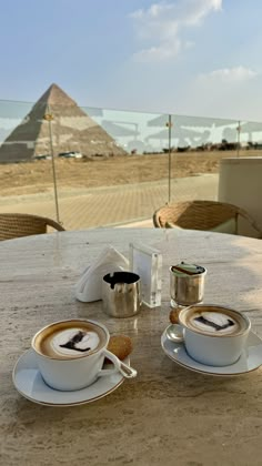 two cups and saucers sitting on top of a table near the pyramids in egypt