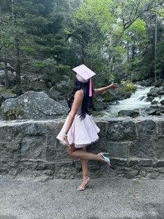 a woman in a graduation cap and gown pointing at the water from a stone wall