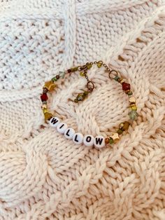 a white knitted blanket with a name bracelet on it and beads hanging from the end