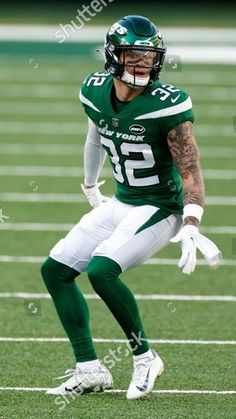 a football player in green and white uniform running on the field with his hands out