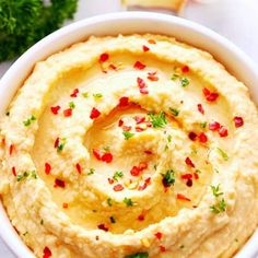 a white bowl filled with hummus and garnished with chopped red pepper sprinkles