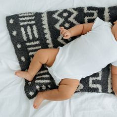 a baby laying on top of a black and white blanket next to a gray rug