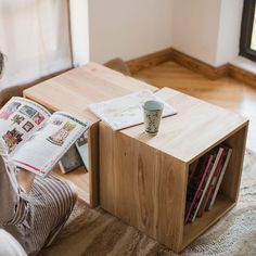 a person sitting on the floor reading a book and drinking coffee from a cup next to an open magazine