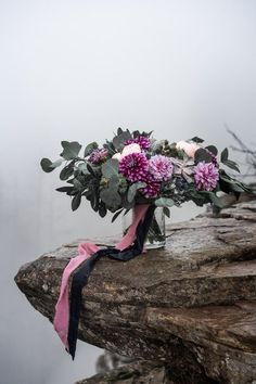 a bouquet of flowers sitting on top of a rock next to the water with fog in the background