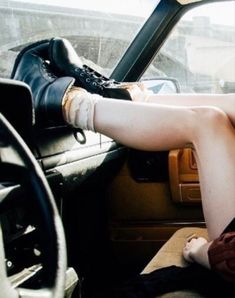 a woman sitting in the driver's seat of a car with her legs up