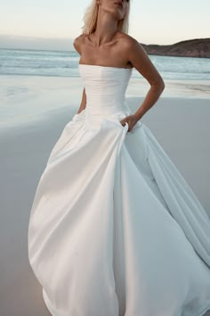 a woman in a white dress standing on the beach with her hands on her hips