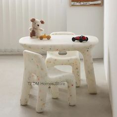 a teddy bear sitting at a white table with two chairs and a toy car on it