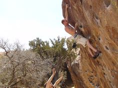 two men climbing up the side of a rock face each other with their hands in the air