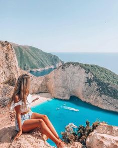 a woman sitting on top of a cliff next to the ocean with an instagram