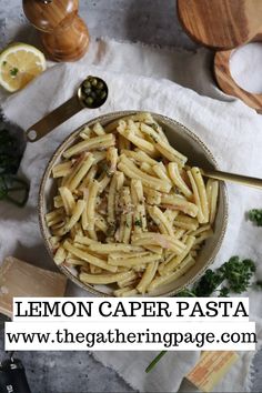 a bowl filled with pasta sitting on top of a table next to lemon wedges