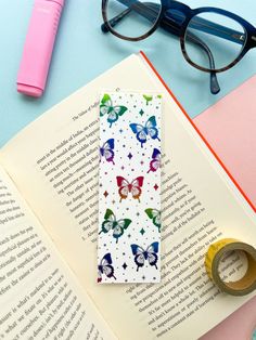 an open book with butterflies on it next to a pair of glasses and a pink pen