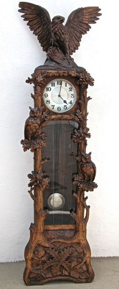 an ornate wooden clock with carved eagle on the front and sides, against a white wall