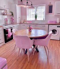 a pink kitchen with white appliances and wooden flooring, including a table that has four chairs around it