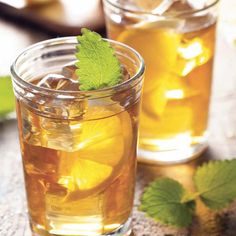 two glasses filled with lemonade and mint on top of a wooden table next to sliced lemons