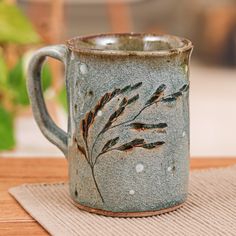 a ceramic mug with some plants painted on the inside and outside, sitting on a place mat