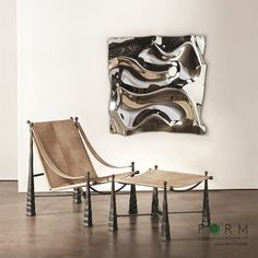 two chairs and a table in front of a wall with an art work on it