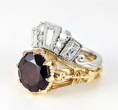 two gold and silver rings with an oval shaped garnet stone surrounded by smaller round diamonds