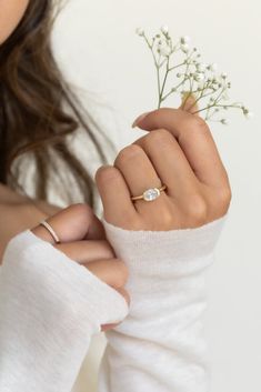 a woman wearing a white sweater holding a flower in her left hand and a diamond ring on her finger