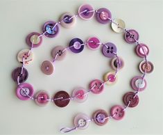 a necklace made out of buttons on a white surface with a purple ribbon around it