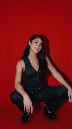 a woman sitting on the ground in front of a red wall with her legs crossed