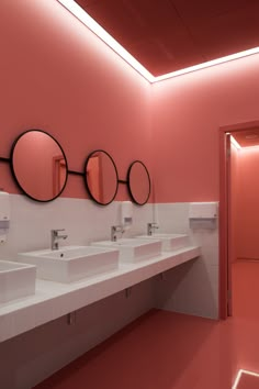 a bathroom with three sinks and mirrors on the wall in front of pink painted walls