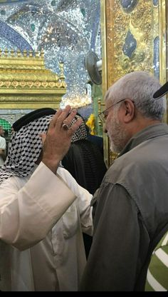 two men standing next to each other in front of a gold and white wall with paintings on it