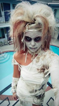 a woman dressed in white with makeup and hair is standing next to a swimming pool