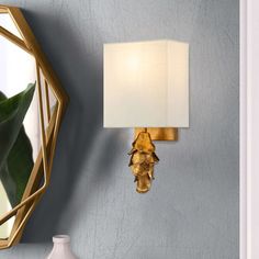 a white vase sitting on top of a table next to a wall mounted mirror and lamp