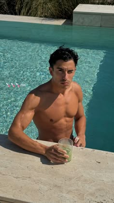 a man sitting next to a swimming pool holding a drink and looking at the camera