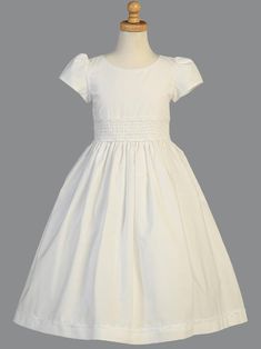 Details Beautiful white cotton tea length communion dress features short sleeves and a scoop neck. Bodice features classic detailing with a smocked waistband. Back has a zipper closure with a sash that ties into a beautiful bow. Available sizes: 6, 7, 8, 10 and 12 Made in the USA by Lito Childrens Wear Tea Length Skirt Outfit, Tea Length Wedding Dress Vintage, Tea Length Bridesmaid Dresses, Girls Communion Dresses, Tea Length Skirt, Baptism Gown, First Communion Dress, First Communion Dresses, Boho Wedding Dress Lace