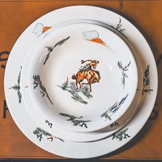 two white plates decorated with an image of a cow and deer on them are sitting on a table