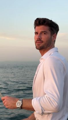 a man standing on the deck of a boat with his hand in his pocket and looking off into the distance