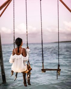 a woman sitting on a swing in the water looking out at the ocean with her back to the camera