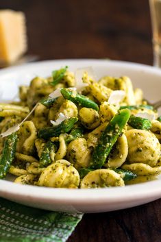 a white bowl filled with pasta and asparagus on top of a wooden table