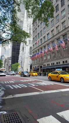 taxi cabs are driving down the street in front of tall buildings with american flags on them