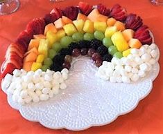 a plate with fruit and marshmallows arranged in the shape of a rainbow