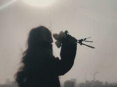 a woman with long hair holding flowers in front of her face and the sun behind her