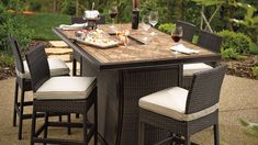 an outdoor dining table with four chairs and two wine glasses on it, in the middle of a garden