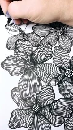 a person is drawing flowers on a piece of paper with black and white lines in the background