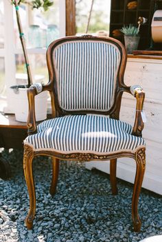 a striped chair sitting on top of gravel next to a white dresser and potted plant