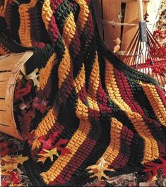 a crocheted blanket sitting on top of a pile of leaves next to a basket