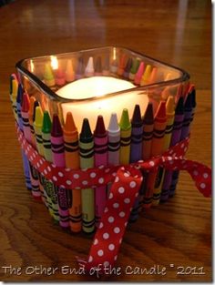 a glass container filled with colored crayons and a lit candle on top of a wooden table