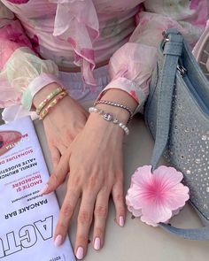 a woman's hands with pink nail polish and bracelets next to a purse