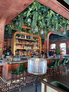 a bar with lots of green chairs and plants hanging from it's ceiling above the bar