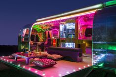 an airstream is lit up at night with colorful lights on the floor and couches