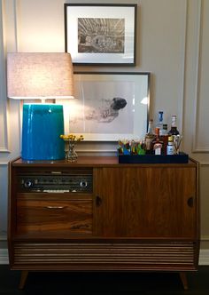 a wooden cabinet with a blue vase on top and a lamp next to it in a room