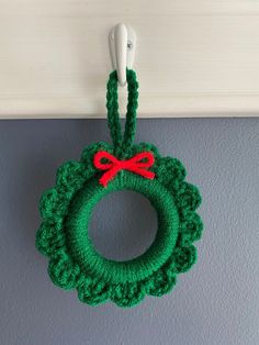 a green crocheted christmas wreath hanging from a hook on the wall with a red bow